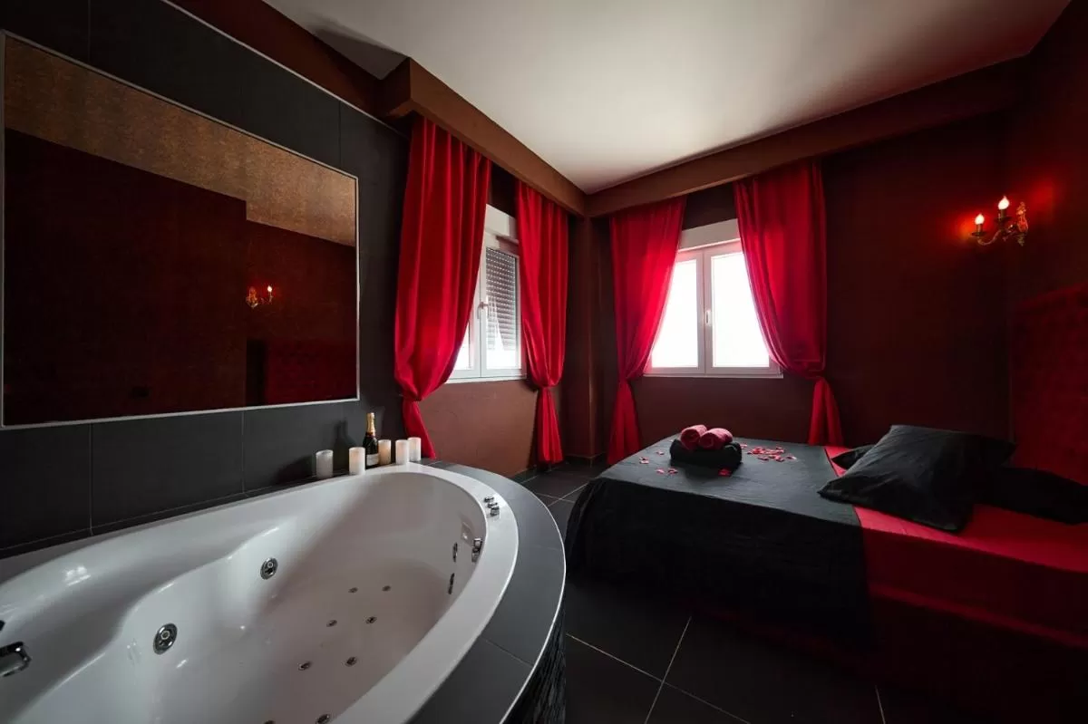 Jacuzzi romántico cerca de la cama con cortinas rojas en Rosa de Pasion Alicante