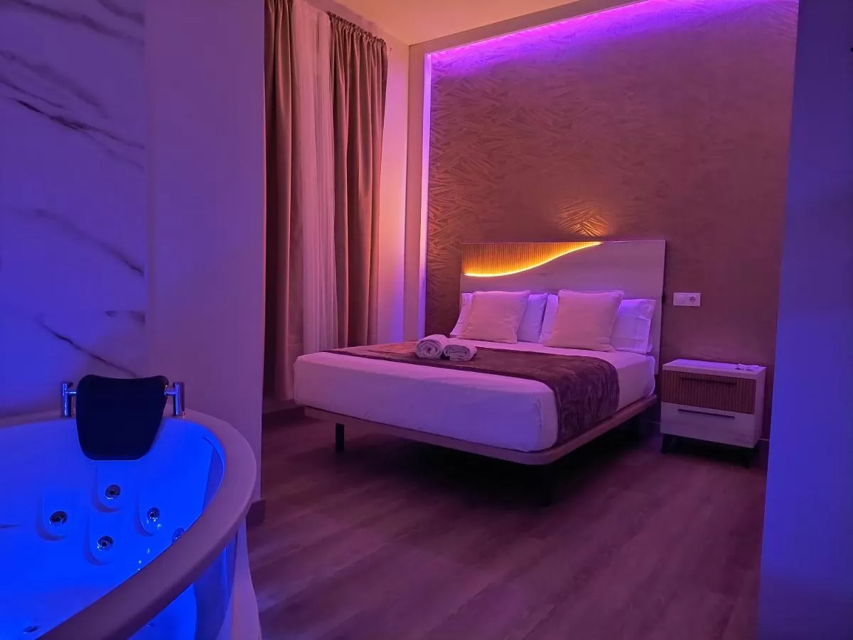 Un dormitorio con una cama con iluminación violeta y jacuzzi en Paradise Suites Madrid,